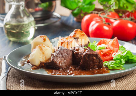 Schweinefleisch Eintopf serviert mit Kartoffeln und Gemüse Salat auf einen Teller. Von der Seite. Stockfoto