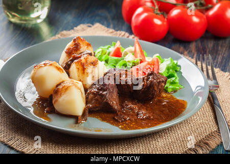 Schweinefleisch Eintopf serviert mit Kartoffeln und Gemüse Salat auf einen Teller. Von der Seite. Stockfoto