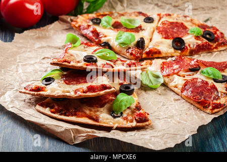 Scheiben Pizza Salami mit Oliven auf einem Papier serviert. Stockfoto