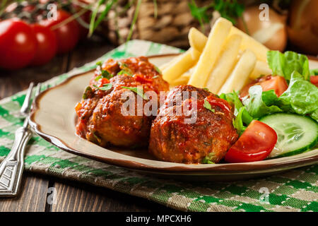 Gebratene Fleischbällchen in Tomatensauce mit Pommes Frites und Salat auf einen Teller Stockfoto