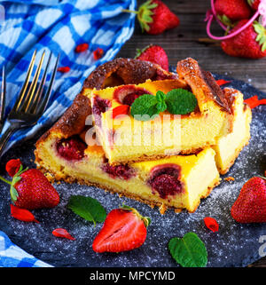 Stück Käsekuchen mit Erdbeeren auf schwarzem Graphit Platte, Ansicht von oben, neben frische reife Beeren Stockfoto