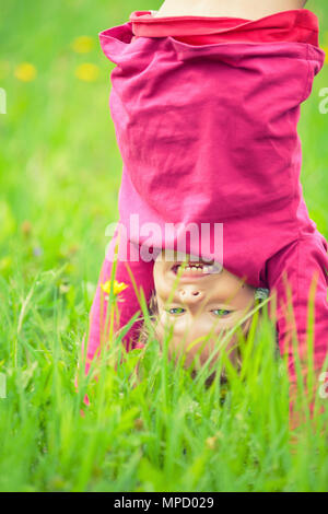 Glückliche kleine Mädchen stehen auf dem Kopf stehend auf dem Rasen im Sommerpark Stockfoto