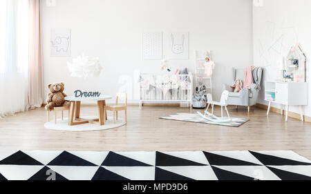 Weißes Schaukelpferd auf Teppich im Zimmer der helles Kind mit kleinem Tisch und geometrischen Teppich Stockfoto
