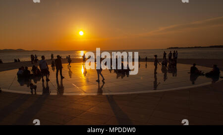 Urlaubern und Touristen bewundern eine glorreiche orange Sonnenuntergang vom photovolt Installation, das Denkmal für die Sonne im Hafen von Zadar Kroatien Stockfoto