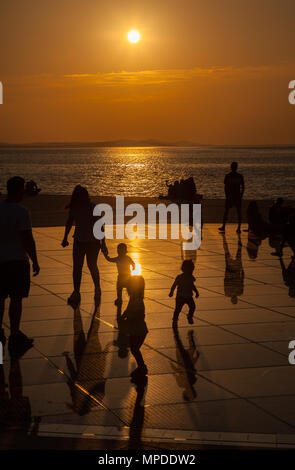 Urlaubern und Touristen bewundern eine glorreiche orange Sonnenuntergang vom photovolt Installation, das Denkmal für die Sonne im Hafen von Zadar Kroatien Stockfoto