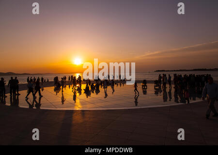 Urlaubern und Touristen bewundern eine glorreiche orange Sonnenuntergang vom photovolt Installation, das Denkmal für die Sonne im Hafen von Zadar Kroatien Stockfoto