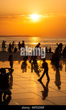 Urlaubern und Touristen bewundern eine glorreiche orange Sonnenuntergang vom photovolt Installation, das Denkmal für die Sonne im Hafen von Zadar Kroatien Stockfoto