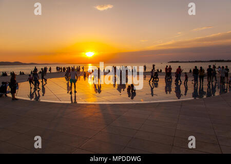 Urlaubern und Touristen bewundern eine glorreiche orange Sonnenuntergang vom photovolt Installation, das Denkmal für die Sonne im Hafen von Zadar Kroatien Stockfoto