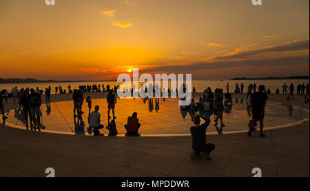 Urlaubern und Touristen bewundern eine glorreiche orange Sonnenuntergang vom photovolt Installation, das Denkmal für die Sonne im Hafen von Zadar Kroatien Stockfoto