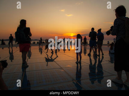 Urlaubern und Touristen bewundern eine glorreiche orange Sonnenuntergang vom photovolt Installation, das Denkmal für die Sonne im Hafen von Zadar Kroatien Stockfoto