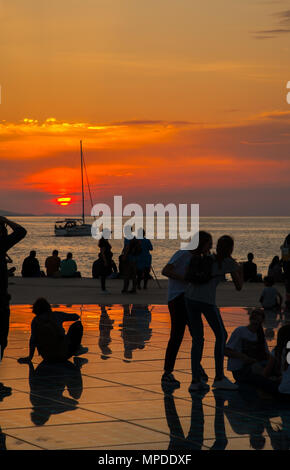 Urlaubern und Touristen bewundern eine glorreiche orange Sonnenuntergang vom photovolt Installation, das Denkmal für die Sonne im Hafen von Zadar Kroatien Stockfoto