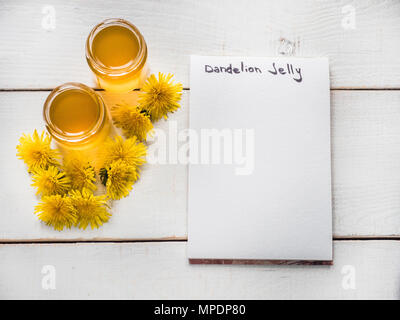 Gelb, hell Löwenzahn, Notebook mit einer leeren Seite für Ihre Inschriften, Blume Honig in einem Gläschen auf einer schönen, weißen, Holztisch. Ansicht von oben, Clo Stockfoto