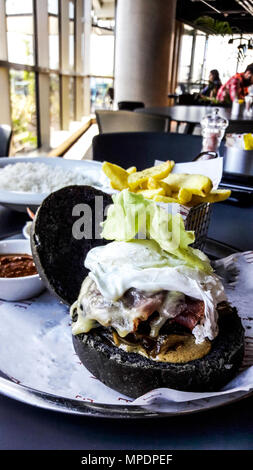 Schwarz Burger mit Speck, Ei, Salat und Kartoffeln im Restaurant. Fast food Konzept. Stockfoto