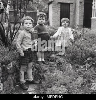 1961, historische, drei Kinder halten Hände beim Spielen im Steingarten eines zurück Garten ein großes Haus in Hanwell, Ealing, London, England. UK. Stockfoto