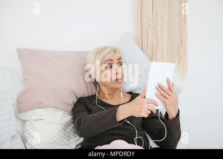 Eine ältere positive Frau verwendet ein Tablet Videos ansehen, Musik hören und mit Freunden über soziale Netzwerke chat Stockfoto