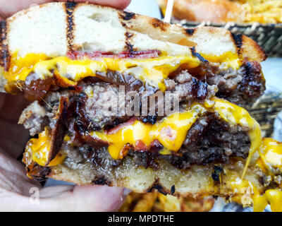 Holding Hamburger mit geschmolzenem Cheddar Käse. Fast Food Konzept. Stockfoto