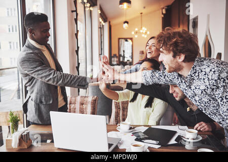 Glückliche junge Unternehmer in Freizeitkleidung im Cafe Tabelle oder im Business Office geben High Fives zu einander, als ob Erfolge feiern oder Starten neues Projekt Stockfoto
