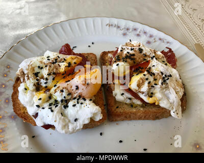 Pochierte Eier auf Toast Brot mit Cheddar Käse, Balsamico, Salat und schwarzem Sesam oder Kreuzkümmel Stockfoto