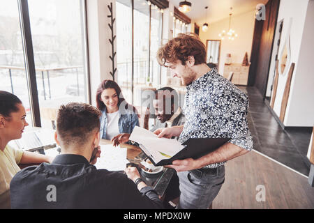 Start Vielfalt Teamarbeit Brainstorming Konzept. Business Team Mitarbeiter teilen Weltwirtschaft Bericht Dokument Laptop. Menschen, die Planung beginnen. Gruppe Junge Hipsters diskutieren Cafe Stockfoto