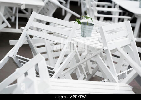 Haufen der invertierten weiße Plastikstühle auf Tabellen in geschlossen Restaurant auf der Terrasse. Schöne Grafik Chaos, interessanten Hintergrund Stockfoto