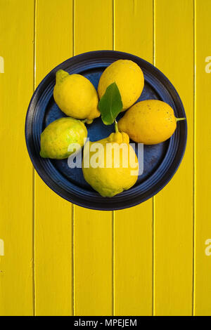 Fünf Zitronen auf Platte und gelb lackierten Holz Hintergrund vertikale kopieren. Stockfoto