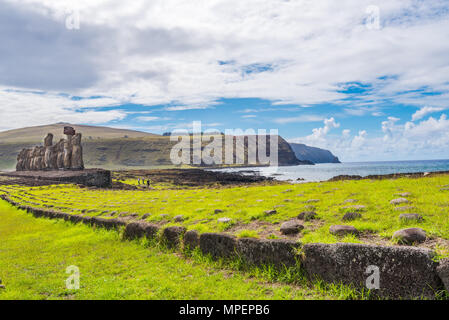 Eine Gruppe von großen Moai Statuen stehen auf einem Altar nach innen vom Ozean entfernt und die Berge im Hintergrund. Stockfoto