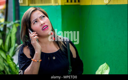 Eine attraktive Filipino asiatische Frau sieht nach oben, in der Kontemplation, während Sie Ihr Handy in den Philippinen. Stockfoto