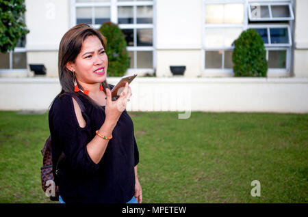 Eine attraktive, hochwertige Asiatische Geschäftsfrau steht im Freien in der Nähe von einem Bürogebäude plaudern auf Ihrem Smartphone in den Philippinen. Stockfoto