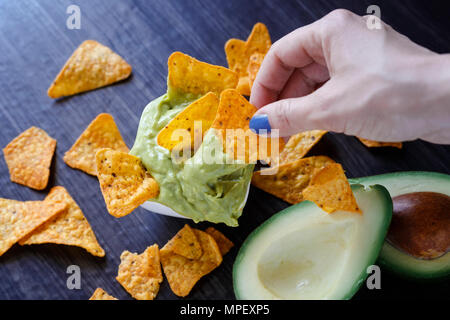 Frau hält einen Tortillachips mit Guacamole dip auf es Stockfoto