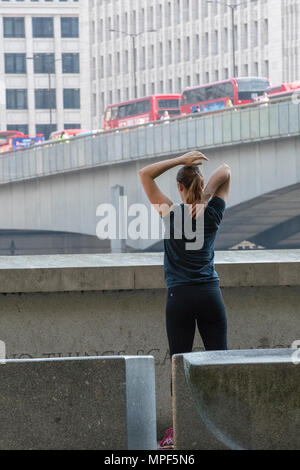 Eine junge Frau, die Ausübung oder Wahrnehmung während der morgendlichen Rush hour in Central London. Stretching Übungen die Muskulatur zu lockern nach der Ausführung. Stockfoto