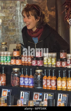 Eine junge Frau von einem Kunden mit einem Stall Verkauf von hot chili Saucen am Borough Market in London lächelnd. Service mit einem Lächeln von einem Markt trader Abschaltdruck Stockfoto