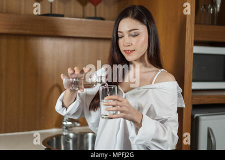 Frau gießt Wasser von der Flasche zum Glas in der Küche Stockfoto