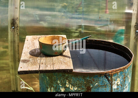 Regenfass gefüllt mit Wasser und Metallpfanne auf Holzbrett an sonnigen Tagen Stockfoto