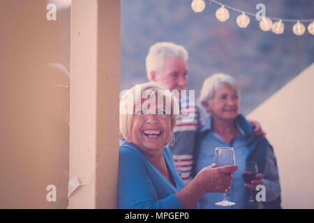 Großes Lächeln für gealterte Frau während der Freizeitaktivitäten auf der Terrasse bei Nacht. Trinken Wein und Spaß an der Party mit Freunden Senior Stockfoto