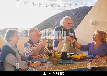 Happy senior Freunden Spaß haben, Wein trinken und am Grill das Abendessen auf der Terrasse Terrasse - reife Menschen, Essen und Lachen zusammen - freudige Ältere lifest Stockfoto