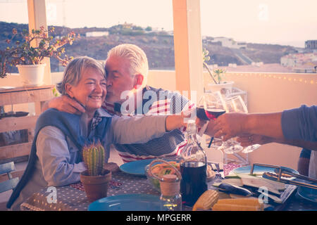 Gruppe von im Alter von älteren Freunde Erwachsene essen und Party schöne Zeit in der Dachterrasse im Freien mit Wein und Essen. Spaß und Küssen du Stockfoto