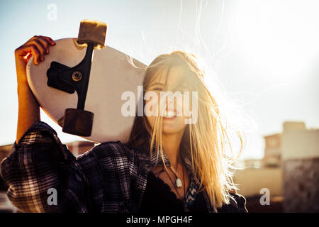 Schön caucasiamo blonde Modell freie Frau mit einem Skateboard in der Sonne Hintergrundbeleuchtung bei Sonnenuntergang. Freiheit und Unabhängigkeit Jugend Konzept auf Teneriffa. Hair Stockfoto