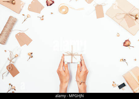 Woman's Hände, die kleine Geschenkbox unter romantischen flach Zusammensetzung der getrocknete Rosen, Geschenke, Bänder und Kerzen auf weißem Hintergrund, Ansicht von oben. Stockfoto