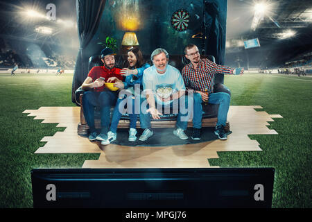 Fußball-Fußball-Fans auf dem Sofa sitzen und Fernsehen in der Mitte eines Fußballfeldes. Stockfoto