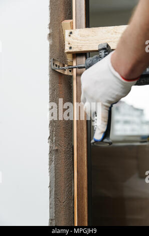 Einbau der Tür. Handwerker zur Festsetzung der Türrahmen mit einem Bohrer. Stockfoto