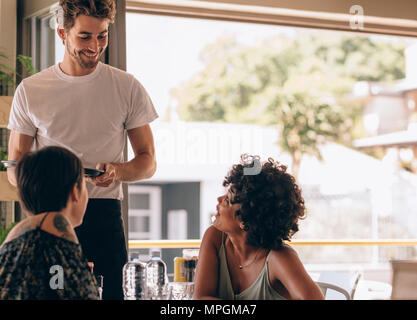 Junge Frau mit einem Freund im Café zu bestellen Kellner. Zwei Frauen im Cafe sitzen, um männliche Kellner. Stockfoto