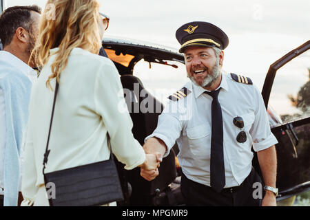 Hubschrauberpilot Händeschütteln mit Frau und lächelt. Paar durch einen privaten Helikopter Reisen mit Pilot Sie begrüßen. Stockfoto