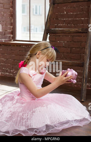 Mädchen 6 Jahre alt in ein rosa Kleid mit einem Sparschwein in seinen Händen. Im Zimmer. Vertikale Framing Stockfoto