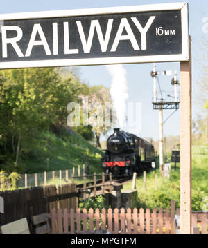 Eisenbahn Schild im Vordergrund. Weichzeichner Dampfmaschine mit Waberndem Dampf nähert sich im Hintergrund. Streckenseitige bei SVR Hampton Loade Station, Shrops. Stockfoto