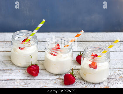 Drei Gläser Joghurt mit Erdbeeren und farbigen Rohre auf einem Holzbrett Stockfoto