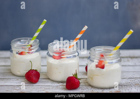 Drei Gläser Joghurt mit Erdbeeren und farbigen Rohre auf einem Holzbrett Stockfoto