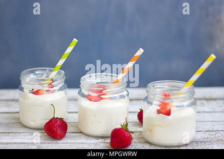 Drei Gläser Joghurt mit Erdbeeren und farbigen Rohre auf einem Holzbrett Stockfoto