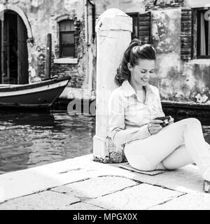 Lächelnde junge Frau sitzt auf der Straße und Überprüfung Fotos in der Kamera in Venedig, Italien Stockfoto