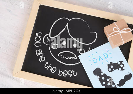 Kinder Zeichnung auf einer Tafel mit Grußkarte und Geschenkverpackung auf Holz- Hintergrund. Vatertag Konzept Stockfoto