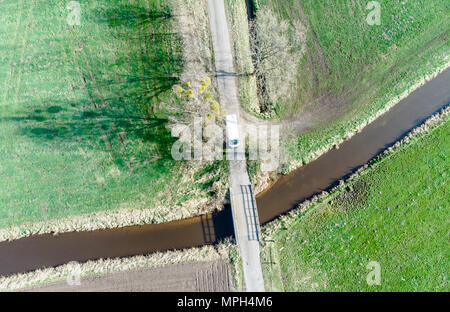 Luftaufnahme eines Baches durch Wiesen und Felder unter einer kleinen Brücke fließt, mit Drone Stockfoto